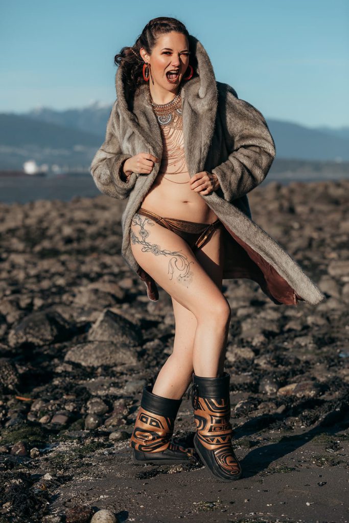 A woman poses in a fur jacket on a beach, wearing