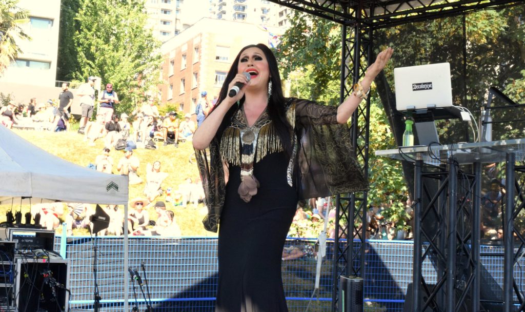 A woman wearing a tight black dress sings into a microphone on stage
