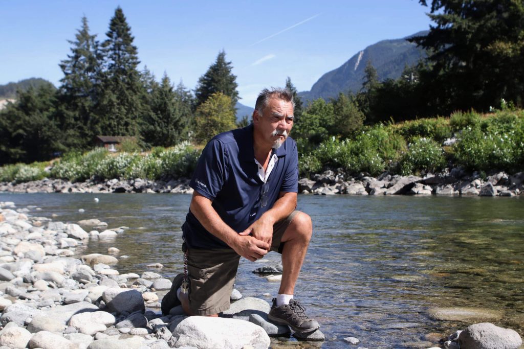 Tim Henry, a Vuntut Gwitchin and Tlingit man kneels along the shore of the Kw'ikw'iya:la River.