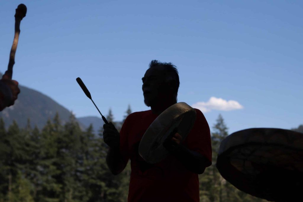 Tim Henry, a Vuntut Gwitchin and Tlingit man drums a song during a ceremony nearby the Kw'ikw'iya:la River in S'olh Temexw, near the site of a Trans Mountain Expansion (TMX) project along the waterway.