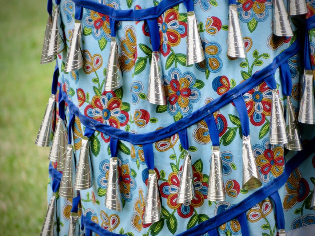 Close up detail of jingle bells on blue flowered patterned dress of young woman Dakota Mishibinijima, who says dancing contributes to her own wellness. 