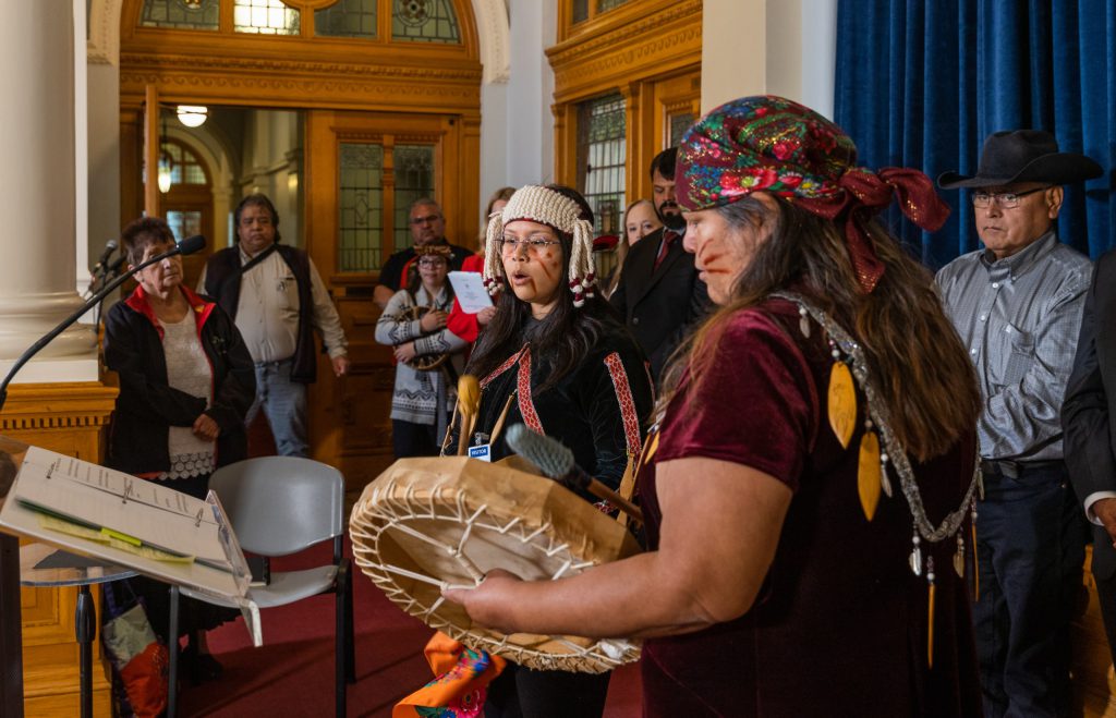 Two people in Coast Salish regalia perform a song inside the B.C. legislature