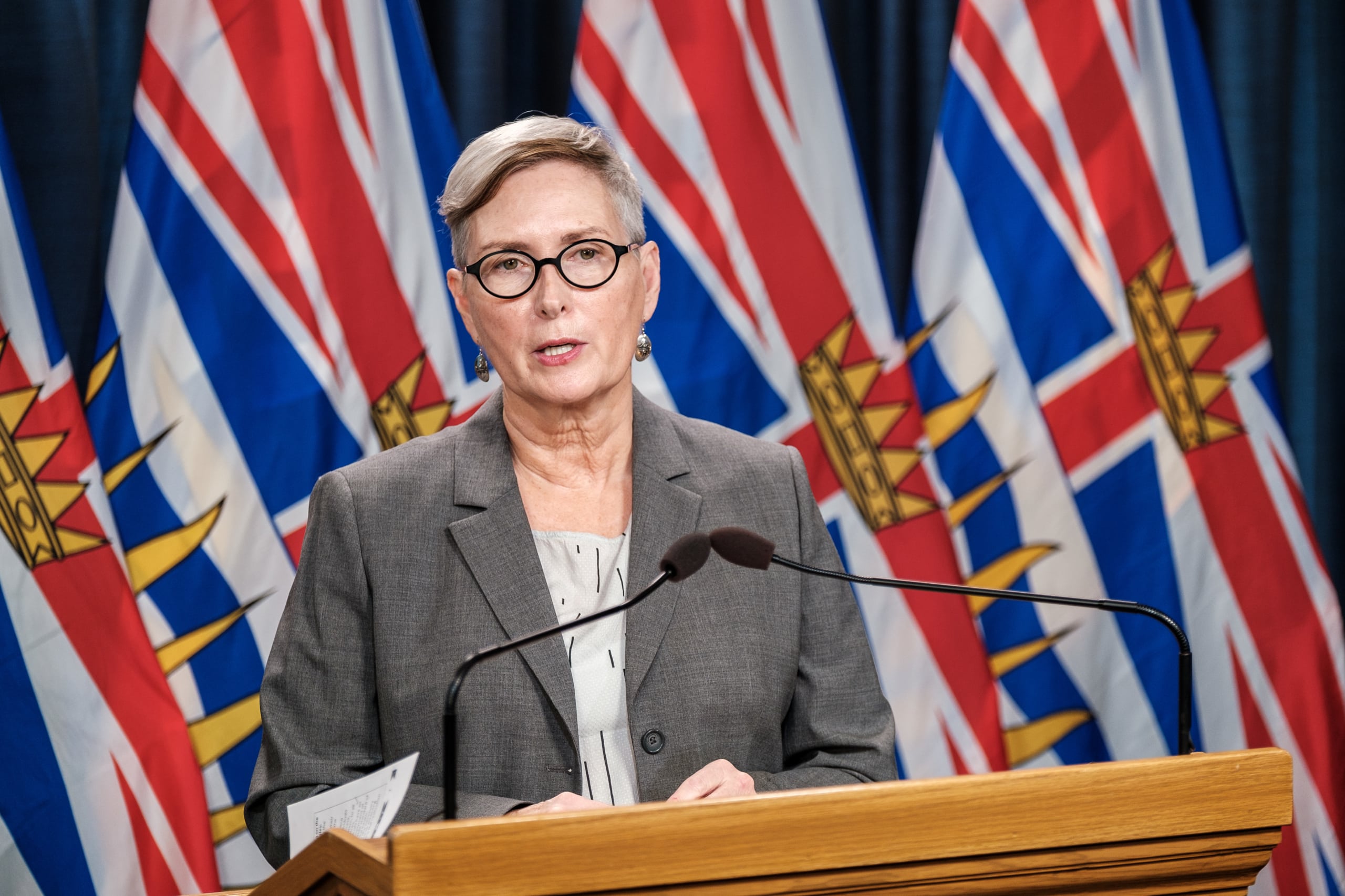 Mary Ellen Turpel-Lafond speaks at a podium with the flags of "British Columbia" behind her.