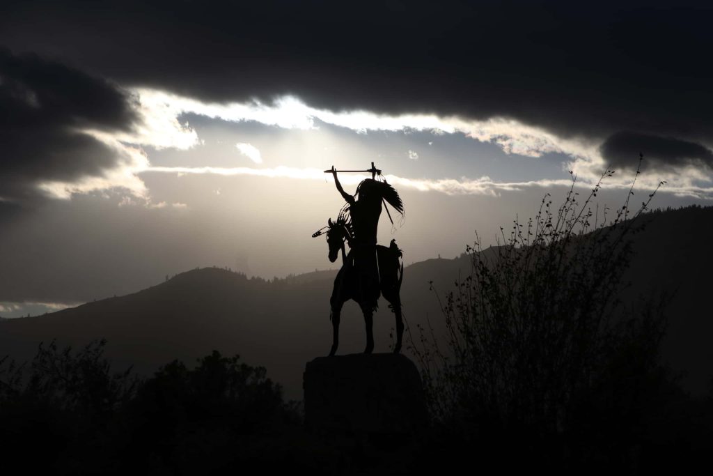 A silhouette of a sculpture of a man on a horse is contrasted by the setting sun