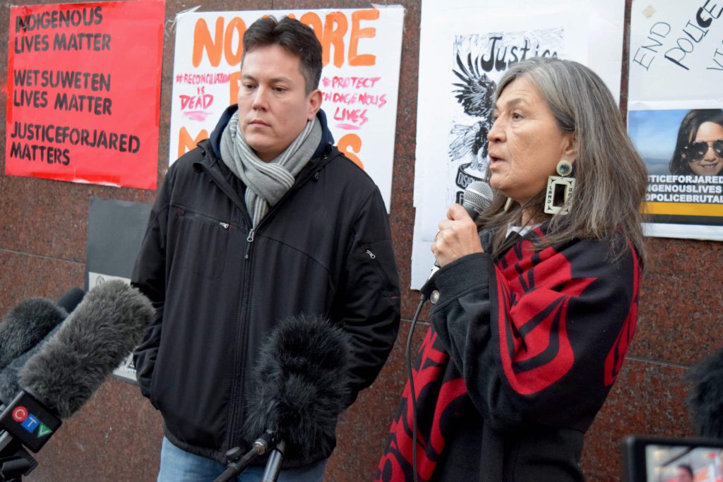 Standing in front of 'justice for Jared' signs, a man and a woman address the media