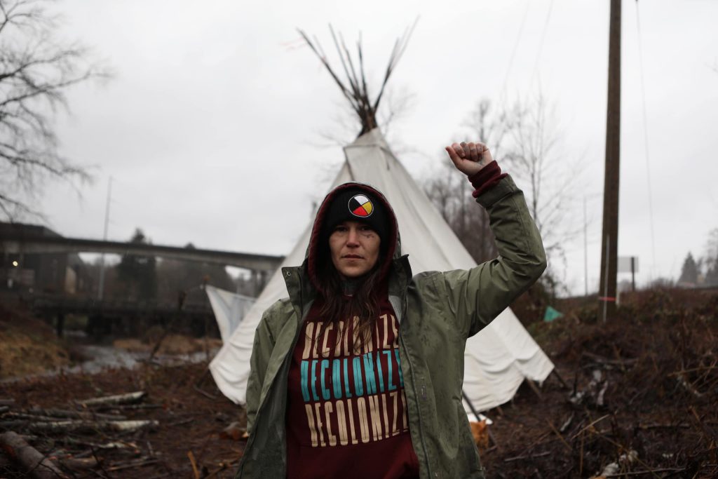 Khursten Bullock, a Cree land defender from Treaty 7 in “Saskatchewan,” poses in front of a tipi that was assembled along the Trans Mountain Pipeline Expansion (TMX) project’s route in “Burnaby” on Jan. 21. Photo by Aaron Hemens