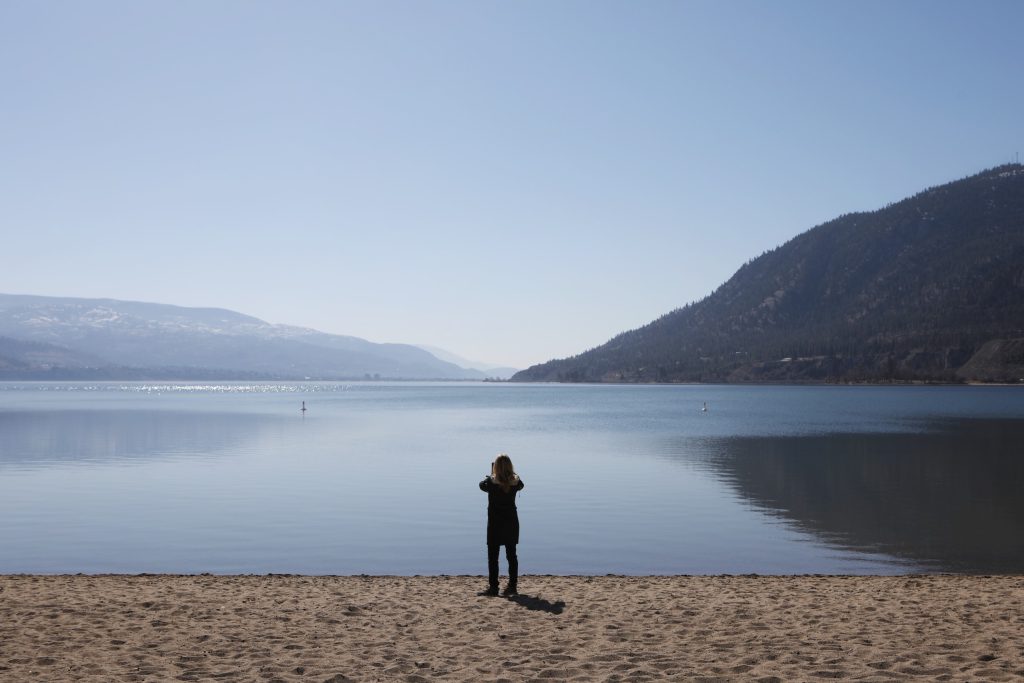 A person attending the Okanagan Nation Alliance’s eighth annual syilx siwɬkʷ (Water) Forum in the district of “Summerland” in syilx homelands takes a picture of kɬúsx̌nítkʷ (Okanagan Lake) from the shore of cnxəlkip (Sun-Oka Beach Park) on March 22. Photo by Aaron Hemens