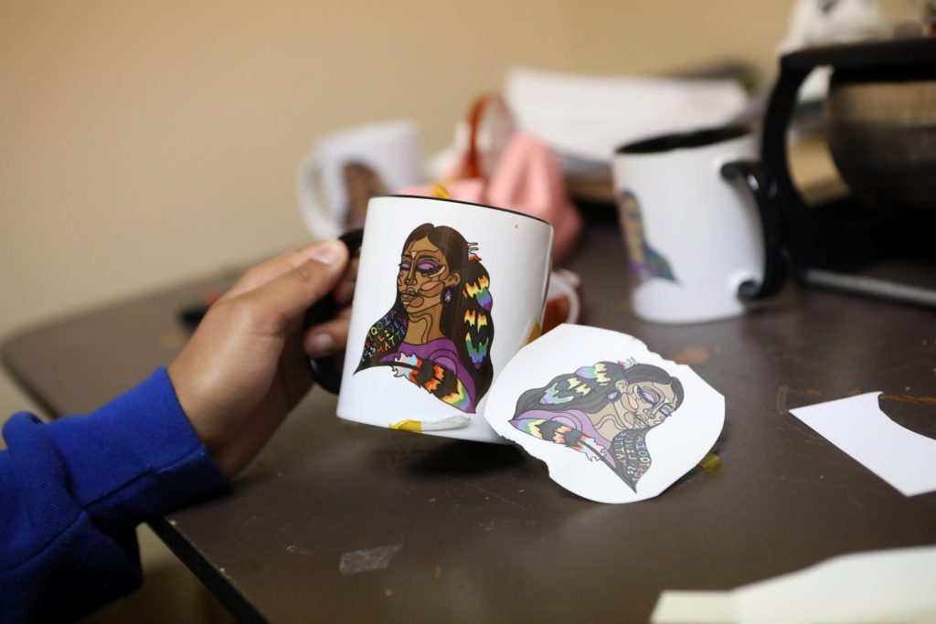 Paige Janvier holds up a mug with Sarah Jones’s Pride design at the Ki-Low-Na Friendship Society in syilx homelands on May 22. Photo by Aaron Hemens