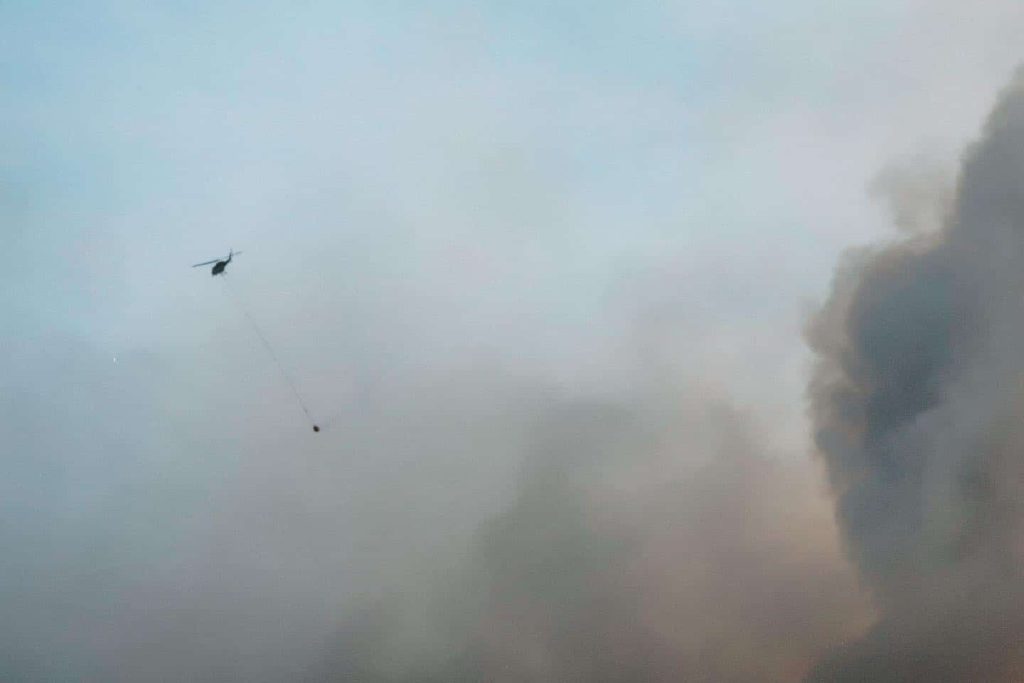 A helicopter releases a water bucket over a fire encroaching on a community in June 2023. Photo by Mike Graeme