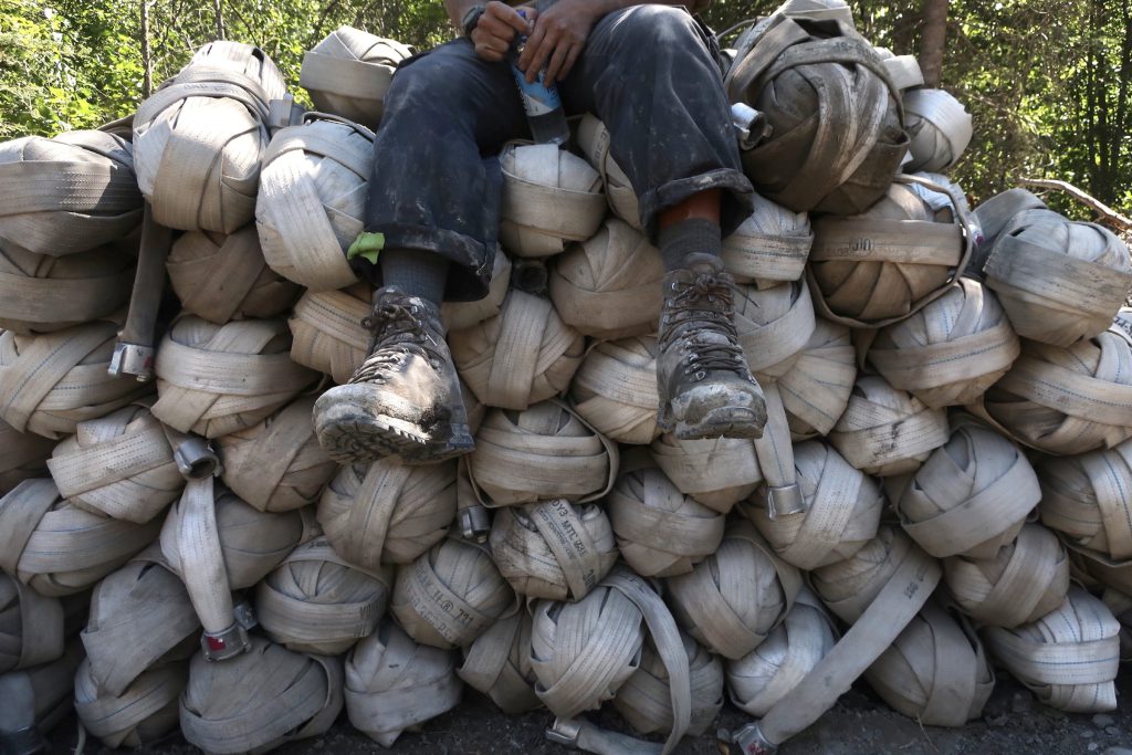 A wildfire fighter sits on a pile of inch-and-a-half hose during the 2023 fire season. Photo by Mike Graeme