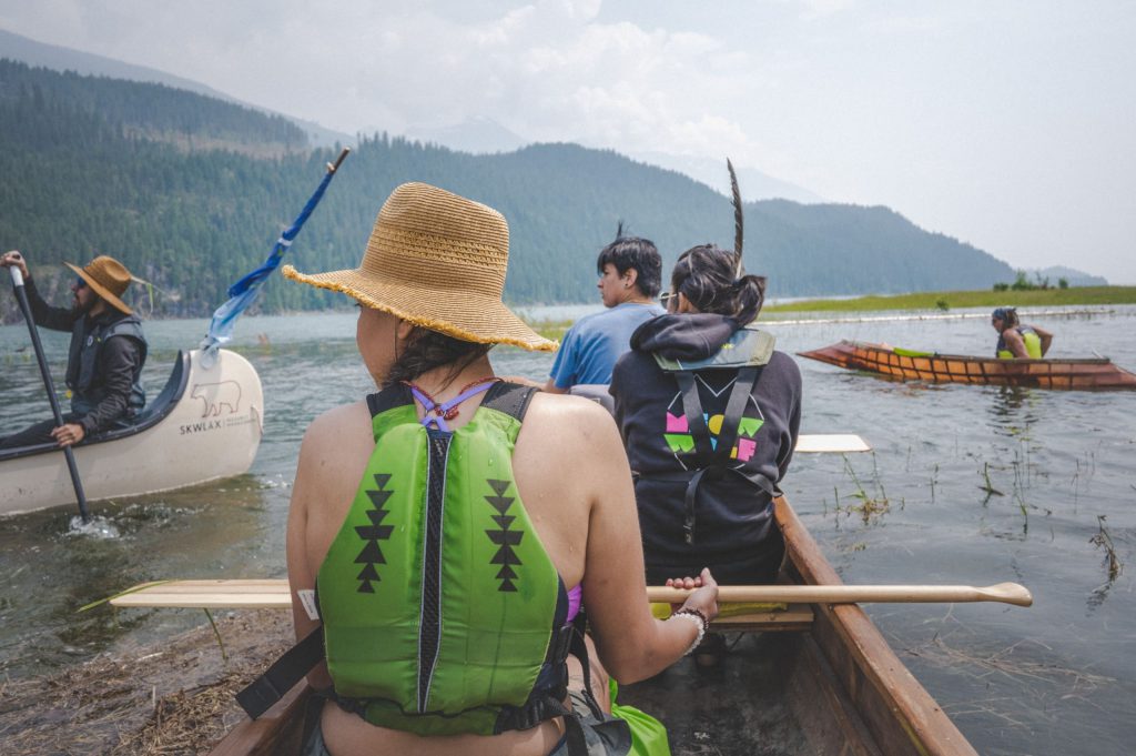 Esquivel (centre) paddles in their northern homelands in a dugout canoe on a smoky day on sn̓ʕaýckst place of the bull trout (Arrow Lakes). Photo by Mike Graeme