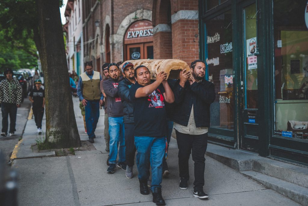 Sinixt people carry a salmon pole carved for them by retired wildlife technician Gary Munro to their new fish and wildlife office in ki’yamələp place of dead trees (Nelson), June 18, 2023. Photo by Mike Graeme