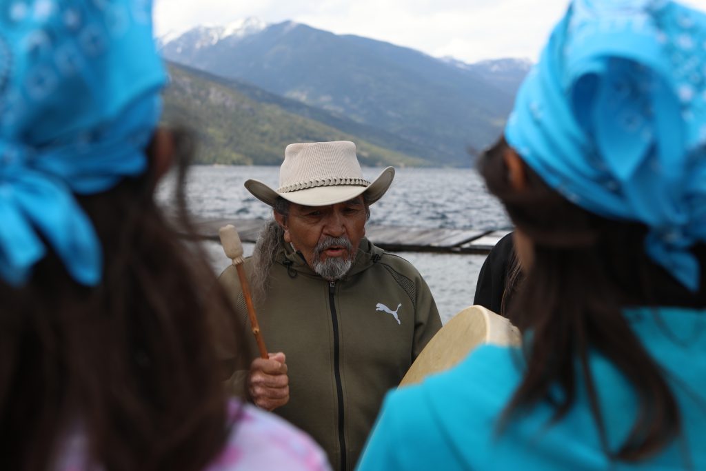 caylx Richard Armstrong, a syilx knowledge-keeper, drums by Slocan Lake in syilx Okanagan territory, during a ceremonial release hosted by the Okanagan Nation Alliance on May 13, 2024. Photo by Aaron Hemens