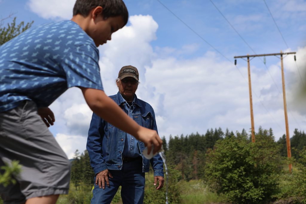 Eric Mitchell, a syilx knowledge keeper, watches as a Youth from Okanagan Indian Band’s Cultural Immersion School releases salmon fry into the Salmon River in syilx Okangan territory during a salmon ceremonial release hosted by the Okanagan Nation Alliance on June 19, 2024. Photo by Aaron Hemens