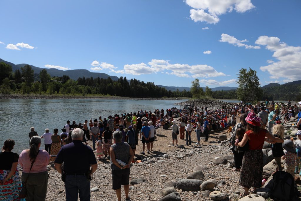 Hundreds of people gather at the banks of nx̌ʷntk’ʷitkʷ (the Columbia River) in snɬuxwqnm (Castlegar) in syilx Okanagan territory during a ceremonial release hosted by the Okanagan Nation Alliance on May 13, 2024. Photo by Aaron Hemens