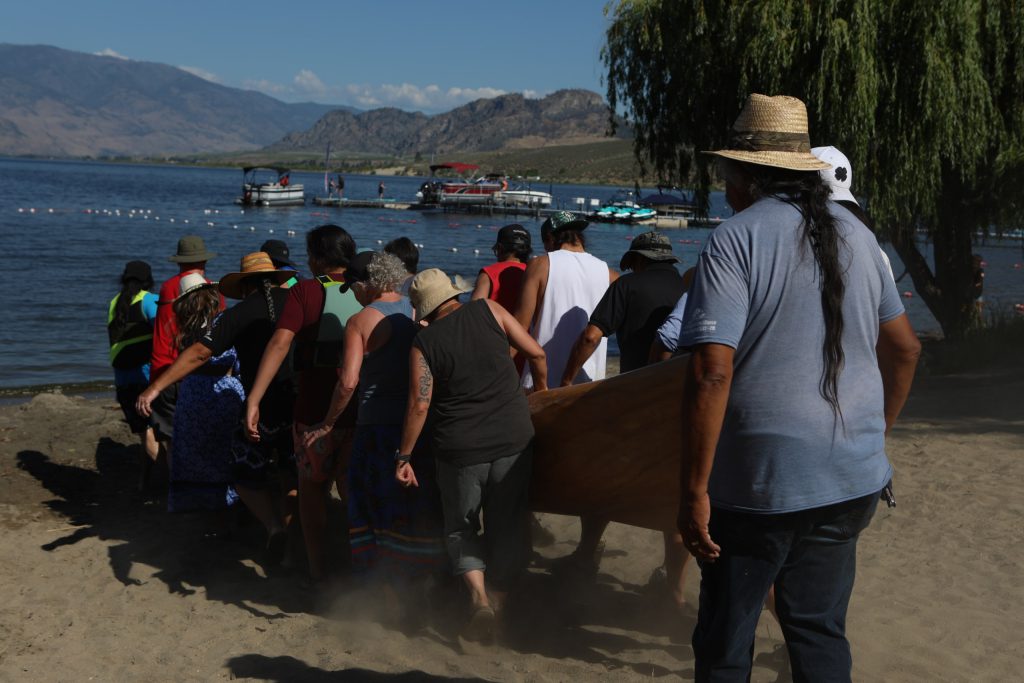 Community members carry a canoe to nk’mip (Osoyoos Lake) in sw̓iw̓s (Osoyoos) prior to the launch of the 2024 Sukʷnaqin canoe journey. Photo by Aaron Hemens