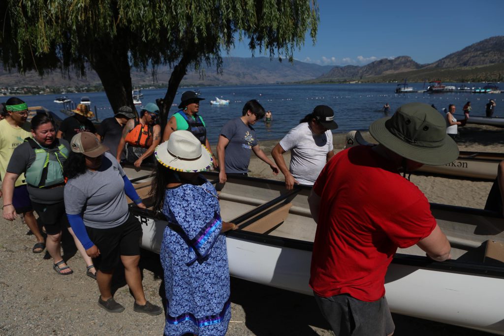 Community members carry a canoe to nk’mip (Osoyoos Lake) in sw̓iw̓s (Osoyoos) prior to the launch of the 2024 Sukʷnaqin canoe journey. Photo by Aaron Hemens