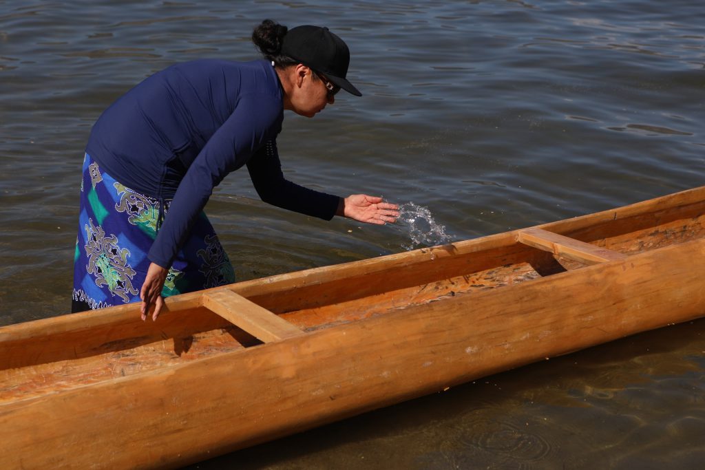 A community member splashes water into a canoe prior to the launch of the 2024 Sukʷnaqin canoe journey. Photo by Aaron Hemens