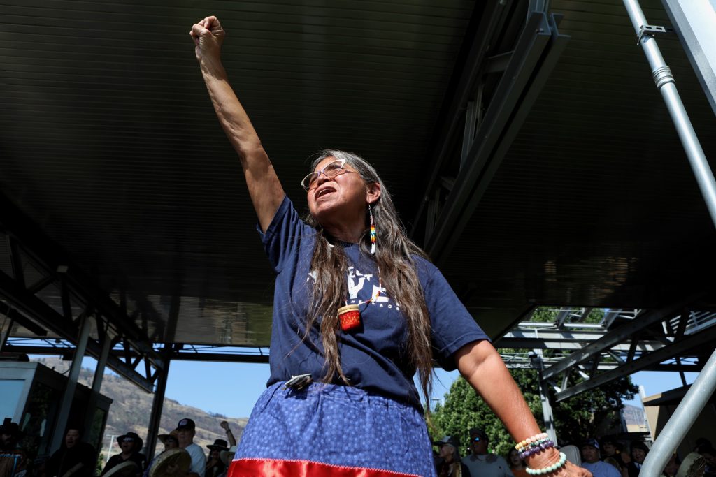 suiki?st Pauline Terbasket, the executive director of the Okanagan Nation Alliance, raises her fist in the air as horseback riders cross into the “U.S.” from “Canada” at the “Osoyoos-Oroville” border in syilx Okanagan homelands on July 20. Photo by Aaron Hemens
