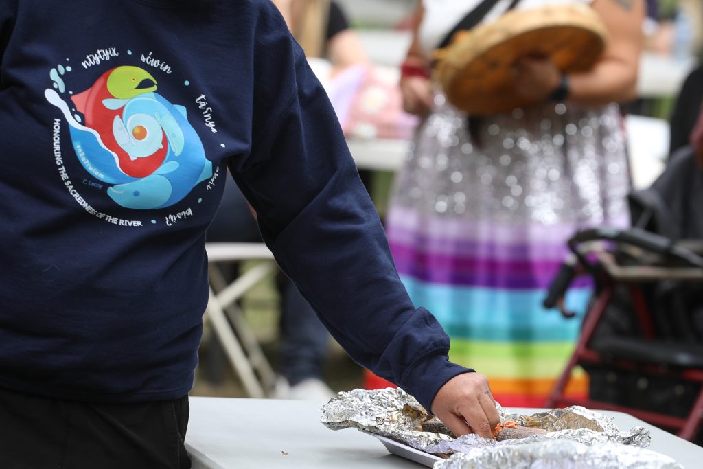 A syilx (Okanagan) community member takes a piece of salmon during the Nation’s 2024 salmon feast and celebration at sx̌ʷəx̌ʷnitkʷ (Okanagan Falls) on Sept. 22. Photo by Aaron Hemens