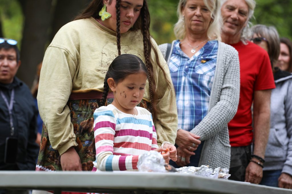 Community members line up and take pieces of salmon during the syilx Nation’s 2024 salmon feast and celebration at sx̌ʷəx̌ʷnitkʷ (Okanagan Falls) on Sept. 22. Photo by Aaron Hemens