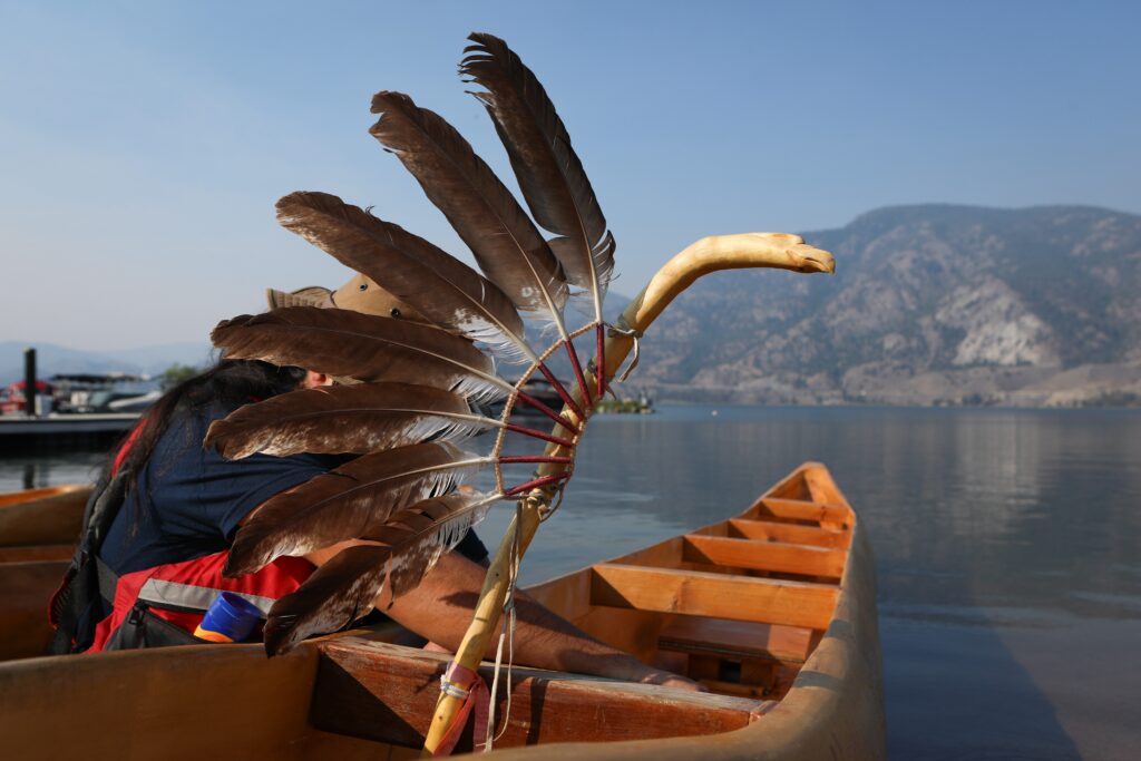 Tristan Marshall ties an eagle staff to the lead dugout canoe at Skaha Lake on July 31, before departing for Okanagan Falls later that morning. The canoe was carved by Herman Edward, who participated in the original journey in 2001. Photo by Aaron Hemens